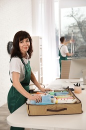 Photo of Professional janitor with organizer and cleaning supplies at table in office
