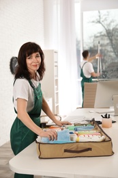 Professional janitor with organizer and cleaning supplies at table in office