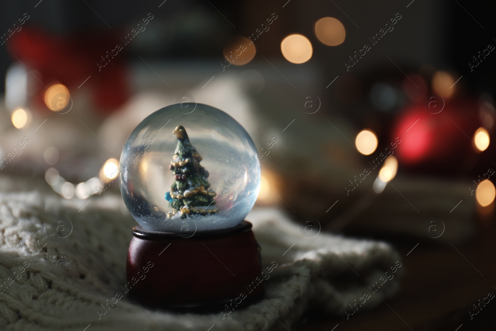 Photo of Christmas snow globe with knitting clothes on blurred background. Space for text