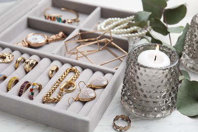 Photo of Elegant jewelry box with beautiful bijouterie and burning candle on white wooden table, closeup