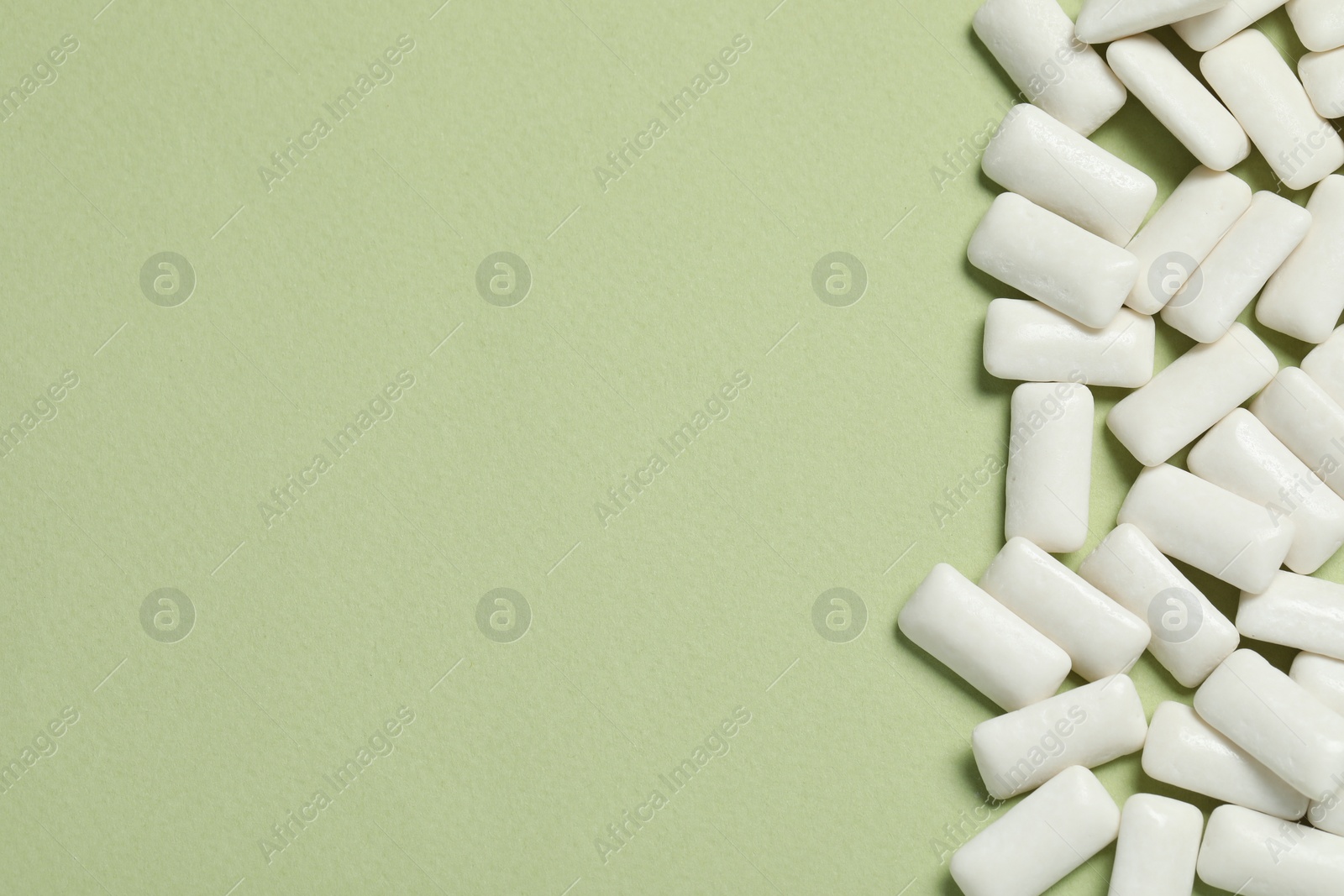 Photo of Tasty white chewing gums on light green background, flat lay. Space for text