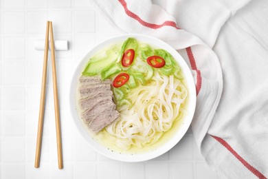 Photo of Bowl of delicious rice noodle soup with celery and meat on white tiled table, flat lay