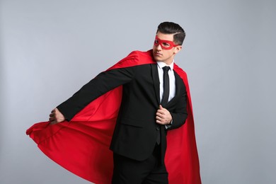 Photo of Businessman wearing superhero cape and mask on grey background