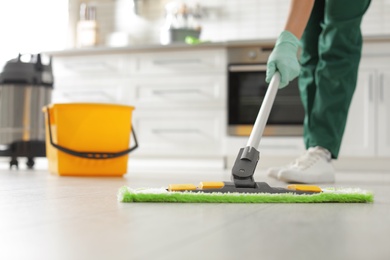 Photo of Professional janitor cleaning floor with mop in kitchen, closeup