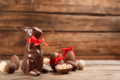 Photo of Chocolate Easter bunny with red bow and eggs on wooden table. Space for text
