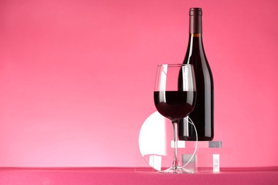 Photo of Stylish presentation of delicious red wine in bottle and glass on pink background. Space for text