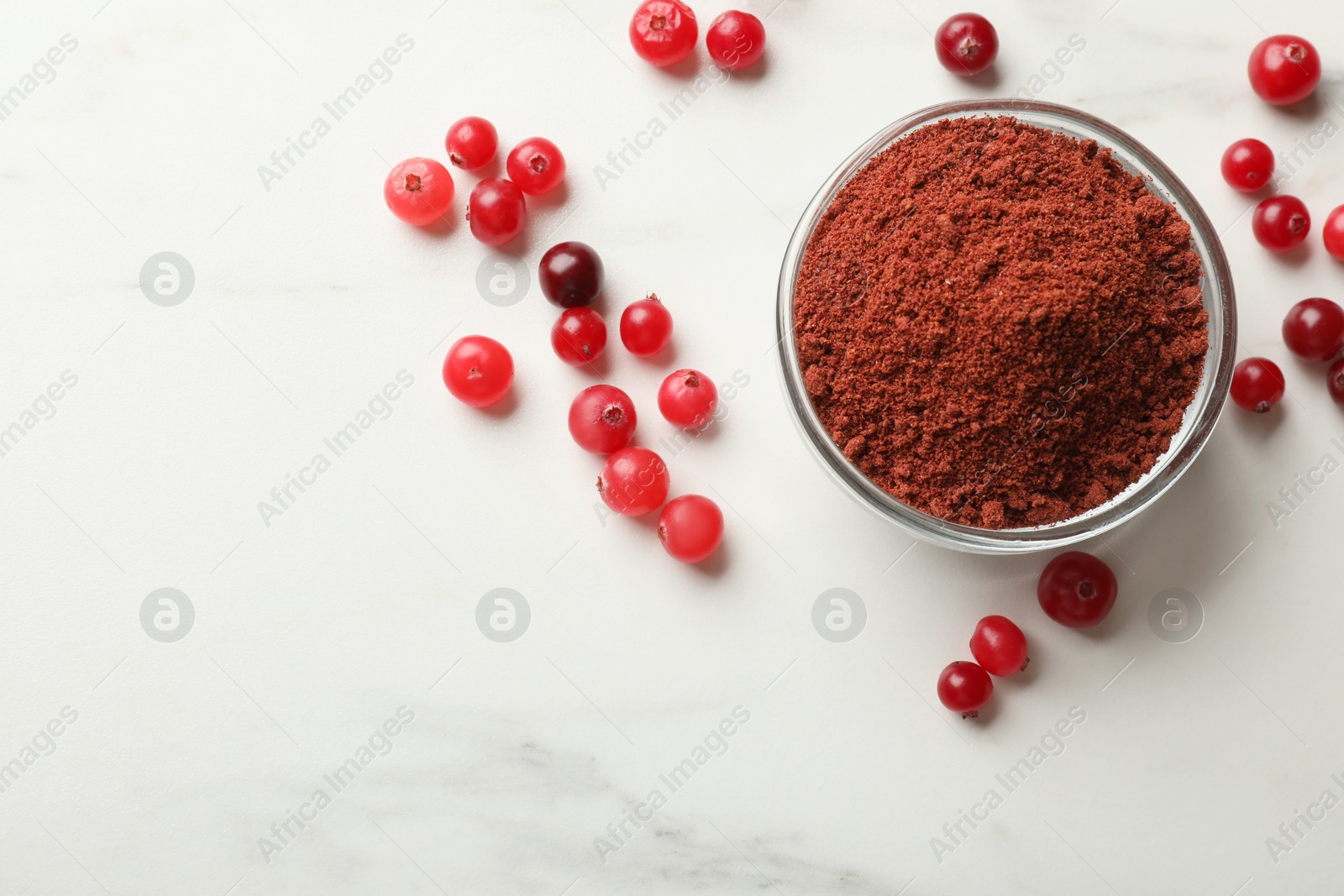 Photo of Dried cranberry powder in bowl and fresh berries on white marble table, top view. Space for text