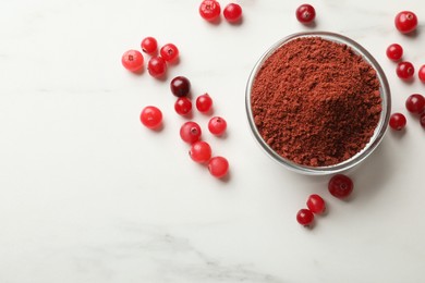 Photo of Dried cranberry powder in bowl and fresh berries on white marble table, top view. Space for text