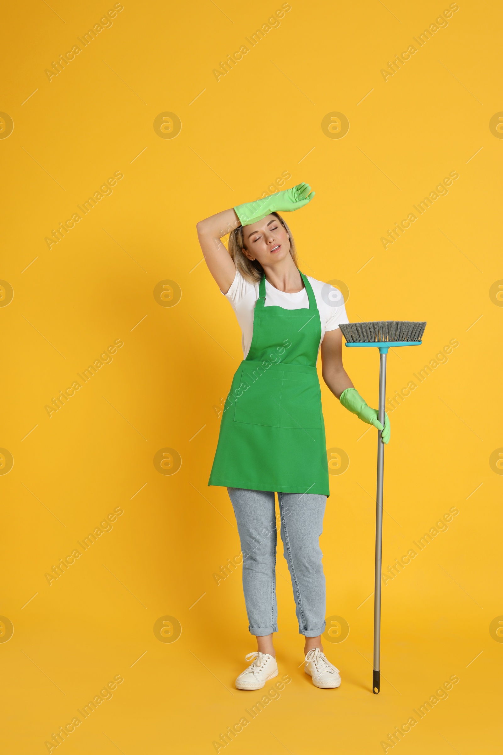 Photo of Tired young woman with broom on orange background