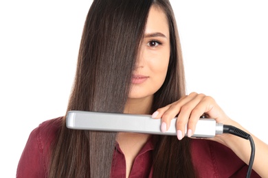 Young woman using hair iron on white background