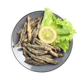Plate with delicious fried anchovies, lemon and lettuce leaves on white background, top view