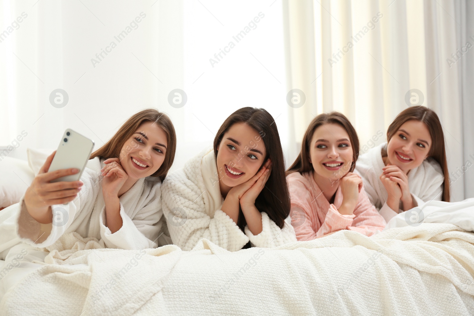 Photo of Beautiful young ladies taking selfie on bed at pamper party. Woman's Day