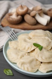 Photo of Plate of delicious dumplings (varenyky) with mushrooms served on grey wooden table, closeup