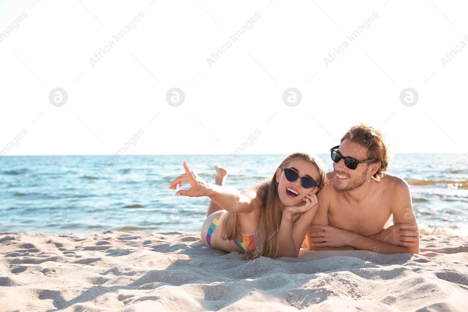 Photo of Happy young couple in sunglasses lying together on beach