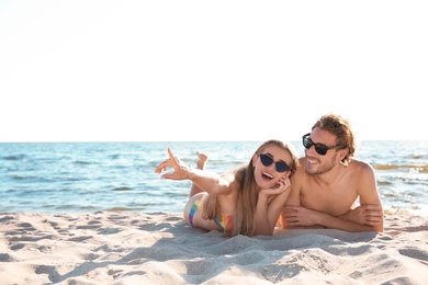 Photo of Happy young couple in sunglasses lying together on beach