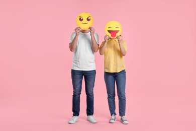 People covering faces with emoticons on pink background