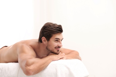 Handsome young man relaxing on massage table against light background, space for text. Spa salon