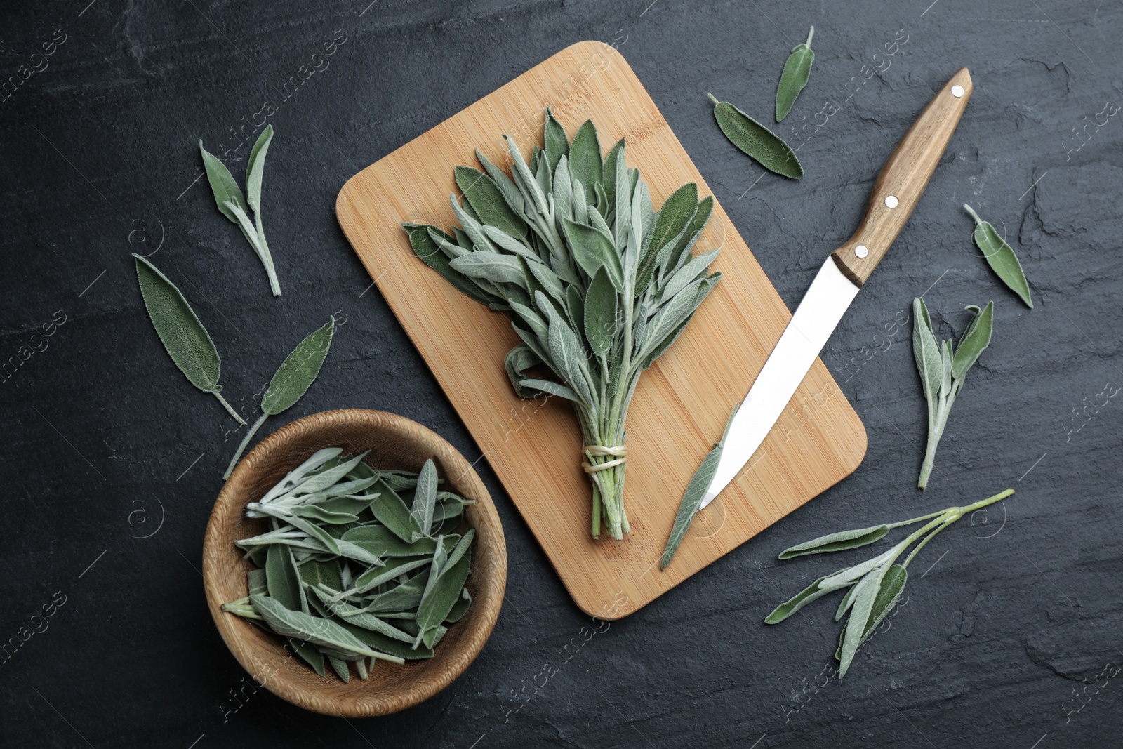 Photo of Fresh green sage with board, knife and bowl on black table, flat lay