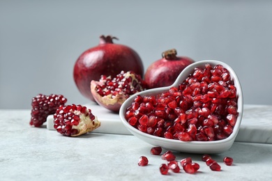 Photo of Bowl with seeds and pomegranates on table against grey background