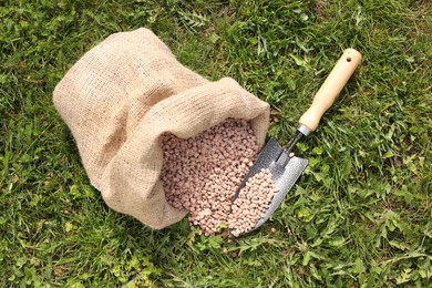 Photo of Granulated fertilizer in sack and shovel on green grass outdoors, top view