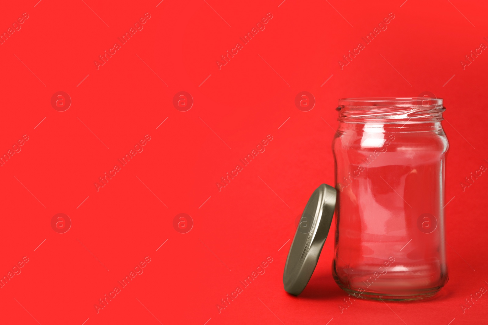 Photo of Open empty glass jar on red background, space for text