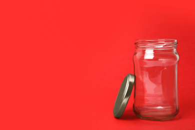 Open empty glass jar on red background, space for text