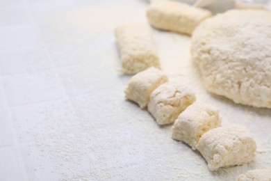 Photo of Making lazy dumplings. Raw dough and flour on white tiled table, closeup. Space for text