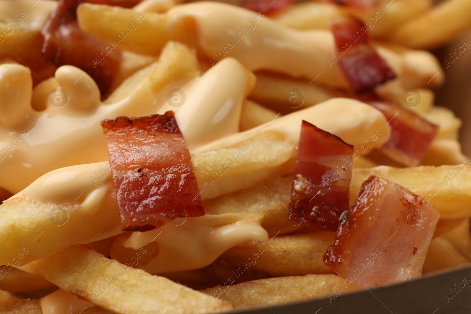 Photo of Tasty potato fries, cheese sauce and bacon in paper container, closeup