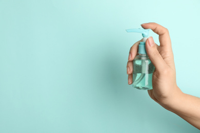Photo of Woman holding antiseptic gel on light blue background, closeup. Space for text