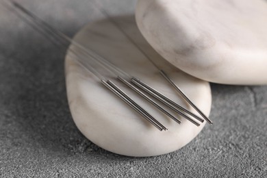 Photo of Acupuncture needles and spa stones on grey table, closeup