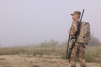 Photo of Man wearing camouflage with hunting rifle and backpack outdoors. Space for text