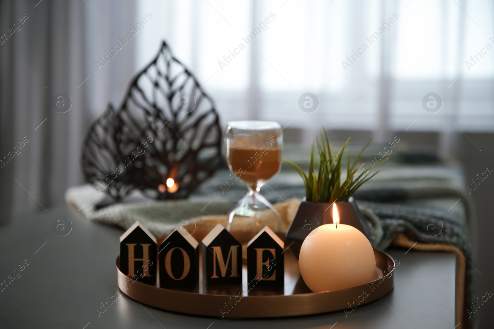 Photo of Tray with burning candle, word HOME and hourglass on table indoors