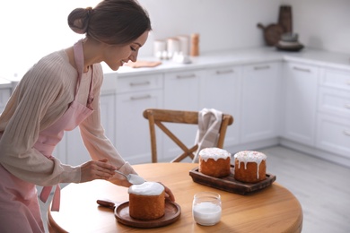 Photo of Young woman decorating traditional Easter cake with glaze in kitchen. Space for text