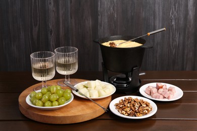 Photo of Fondue pot with tasty melted cheese, forks, wine and different snacks on wooden table