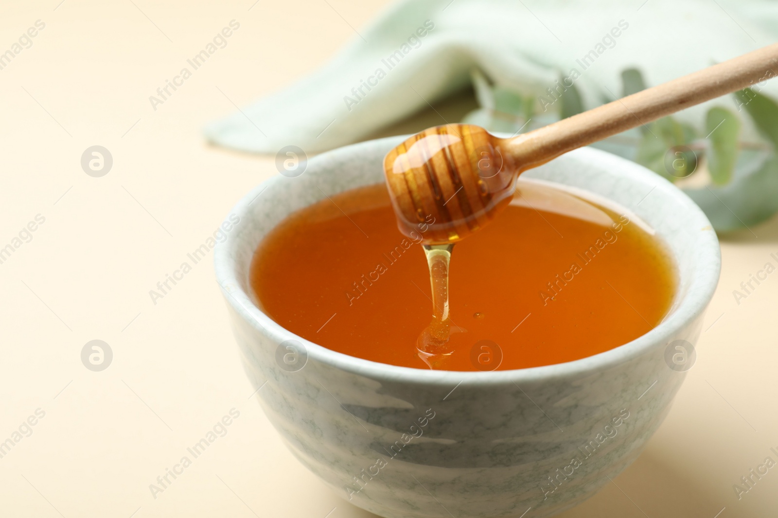 Photo of Bowl of organic honey and dipper on beige background