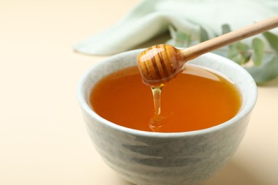 Photo of Bowl of organic honey and dipper on beige background