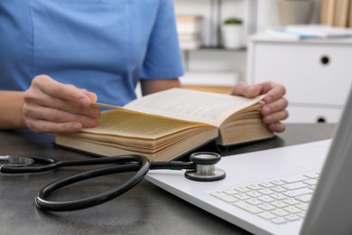 Photo of Medical student in uniform studying at table indoors, closeup