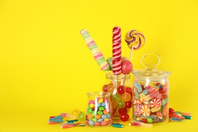 Photo of Jars with different delicious candies on yellow background. Space for text