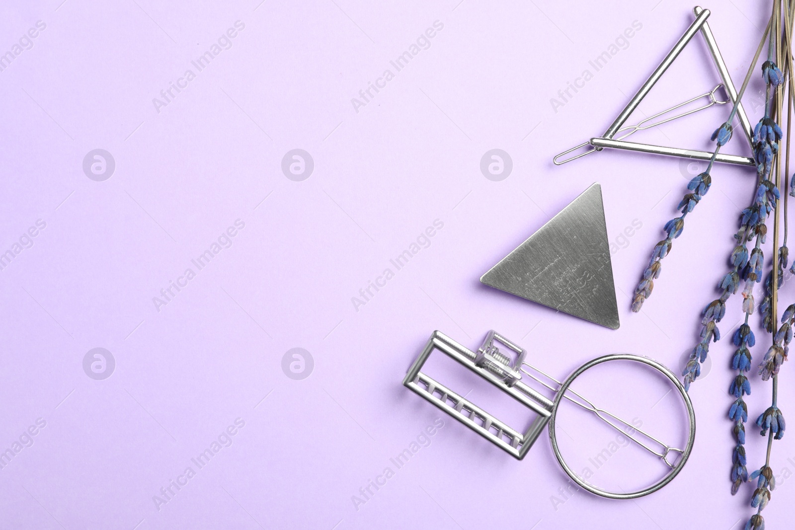 Photo of Stylish hair clips and flowers on violet background, flat lay. Space for text