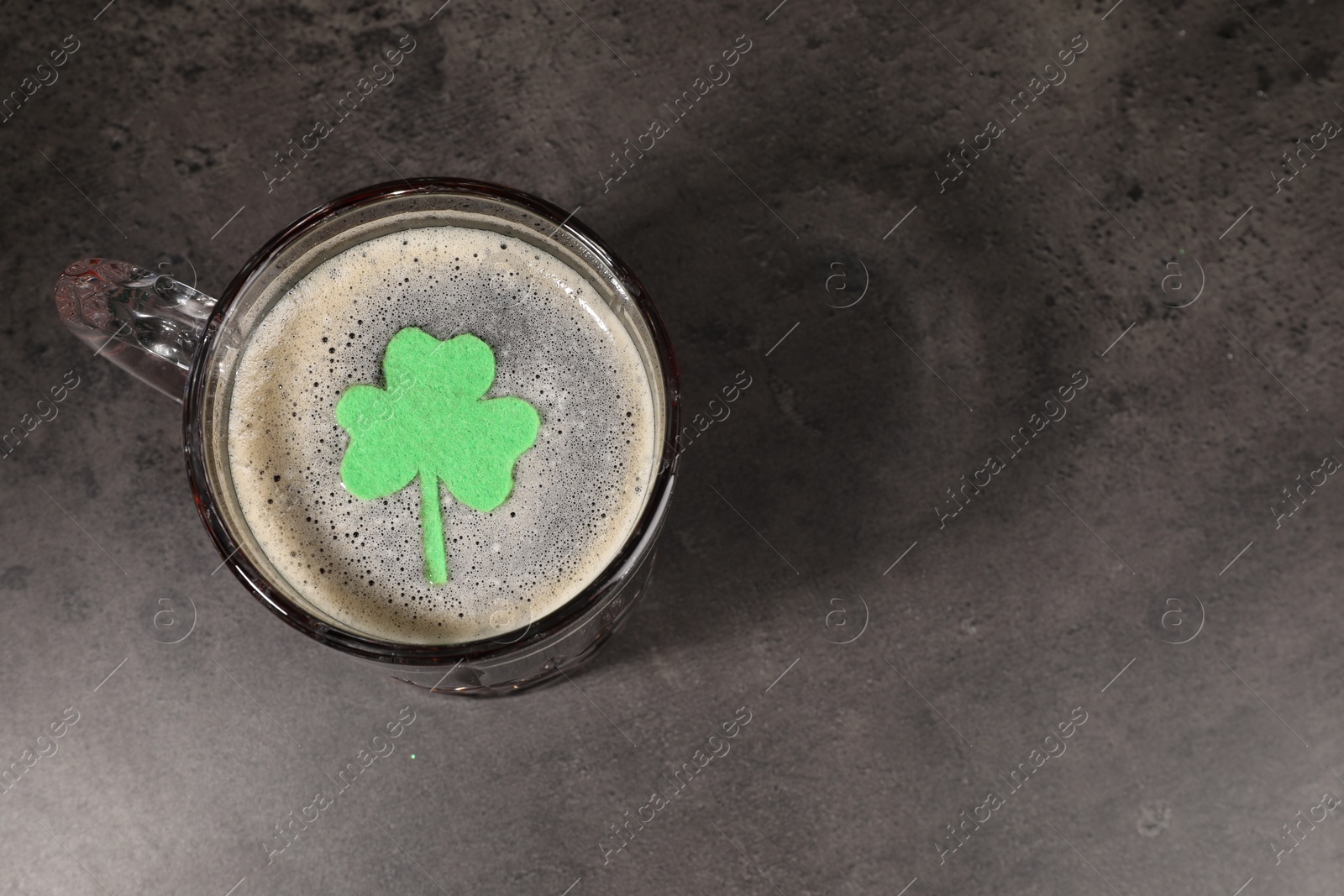 Photo of St. Patrick's day celebration. Green beer with decorative clover leaf on grey table, top view. Space for text