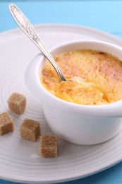 Photo of Delicious creme brulee in bowl served on light blue table, closeup