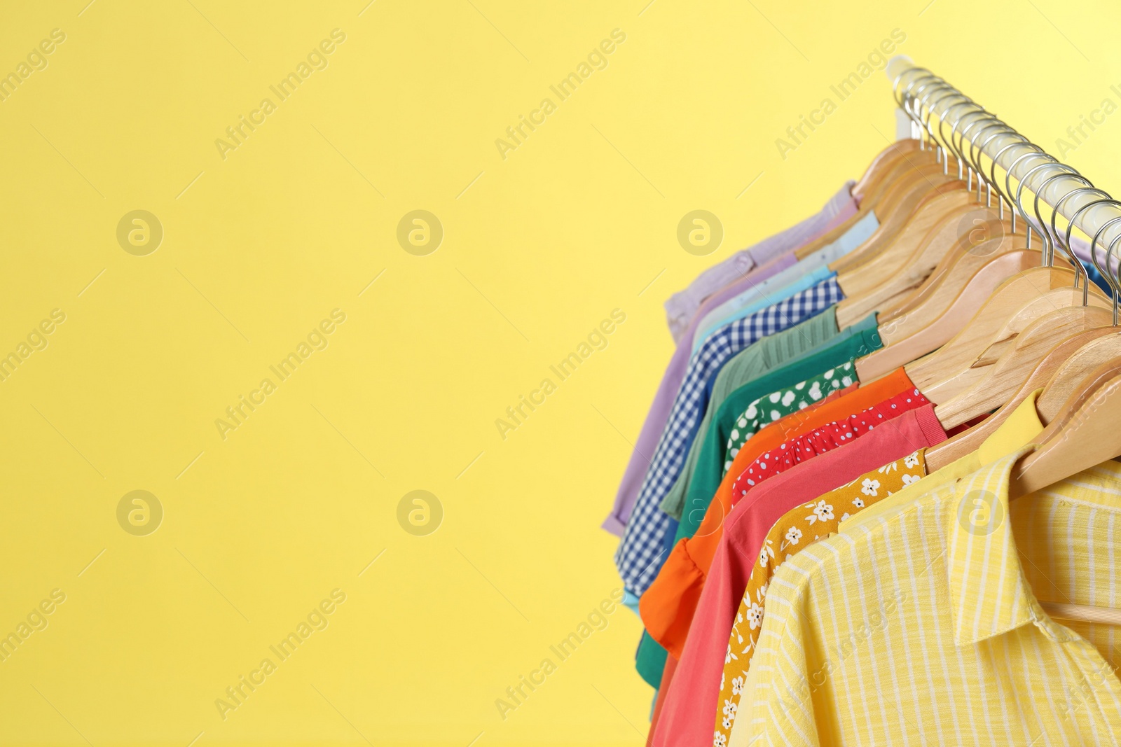 Photo of Bright clothes hanging on rack against yellow background, space for text. Rainbow colors