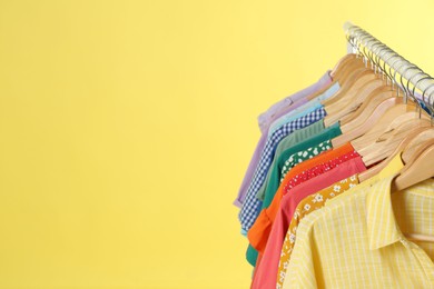 Photo of Bright clothes hanging on rack against yellow background, space for text. Rainbow colors