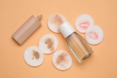 Photo of Bottle of makeup remover, foundation and dirty cotton pads on pale orange background, flat lay