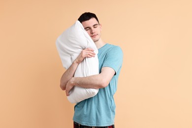 Man in pyjama holding pillow and sleeping on beige background