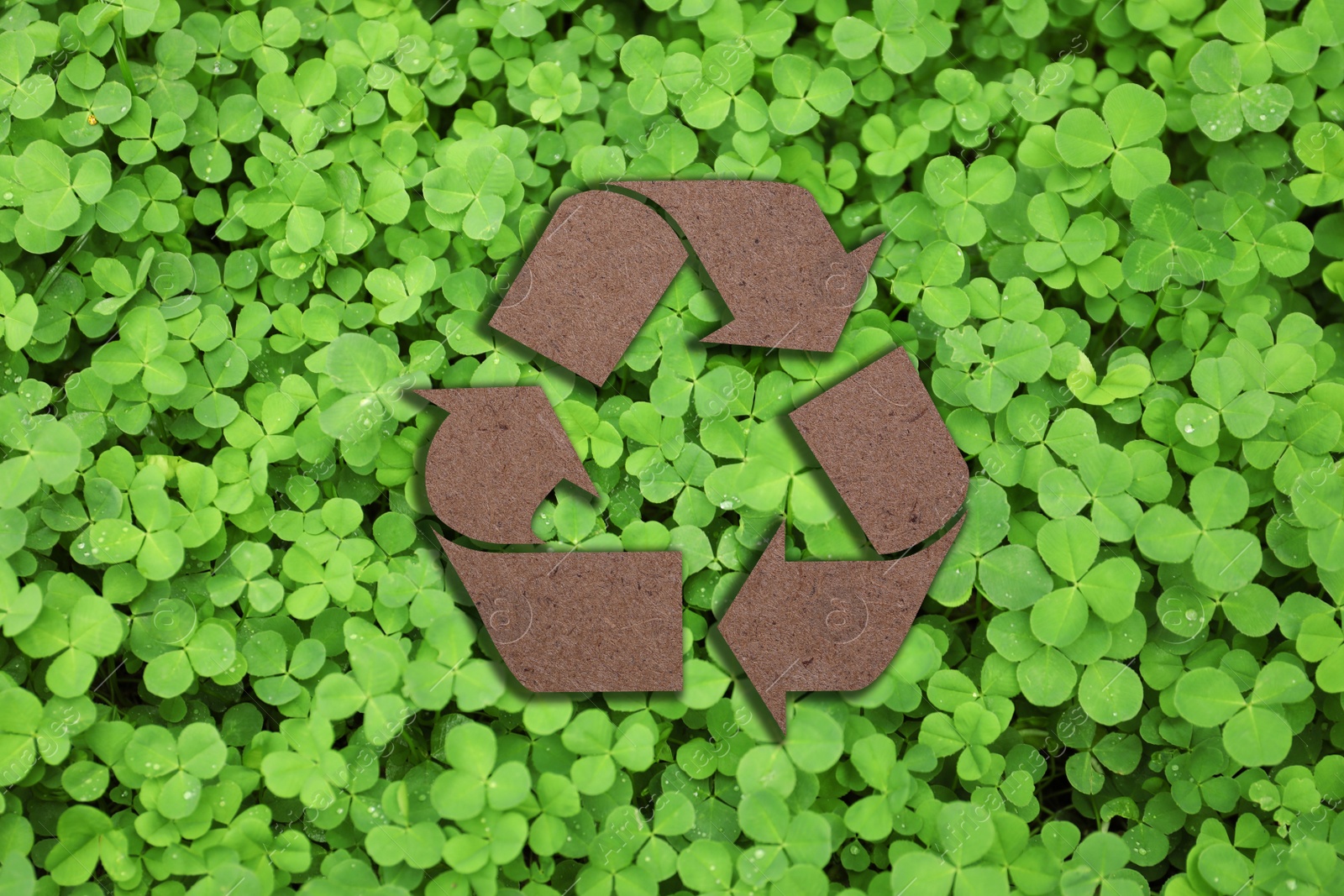 Image of Recycling symbol cut out of kraft paper and fresh green leaves on background