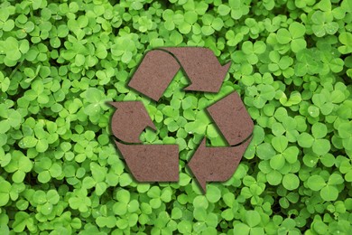 Image of Recycling symbol cut out of kraft paper and fresh green leaves on background