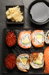 Photo of Delicious sushi rolls, soy sauce and ginger on black table, flat lay