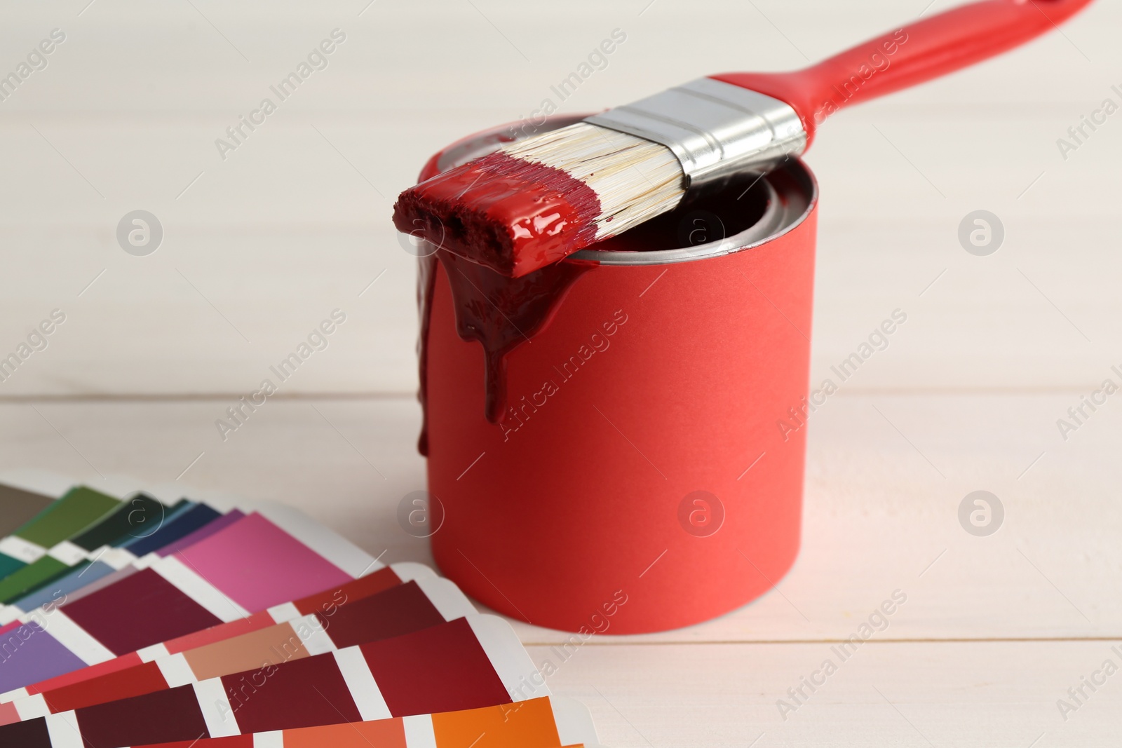 Photo of Can of red paint with brush and palette on white wooden background