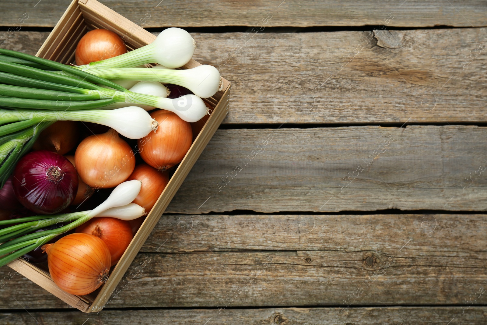 Photo of Crate with different kinds of onions on wooden table, top view. Space for text